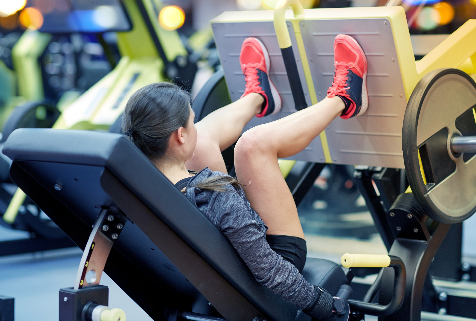 woman flexing muscles on leg press machine in gym